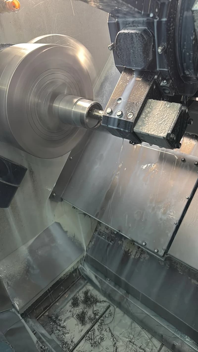 Eine Drehmaschine bearbeitet ein Metallstück, wobei Kühlmittel und Metallspäne entstehen. Die Maschine ist in Betrieb und das Metallstück dreht sich schnell.