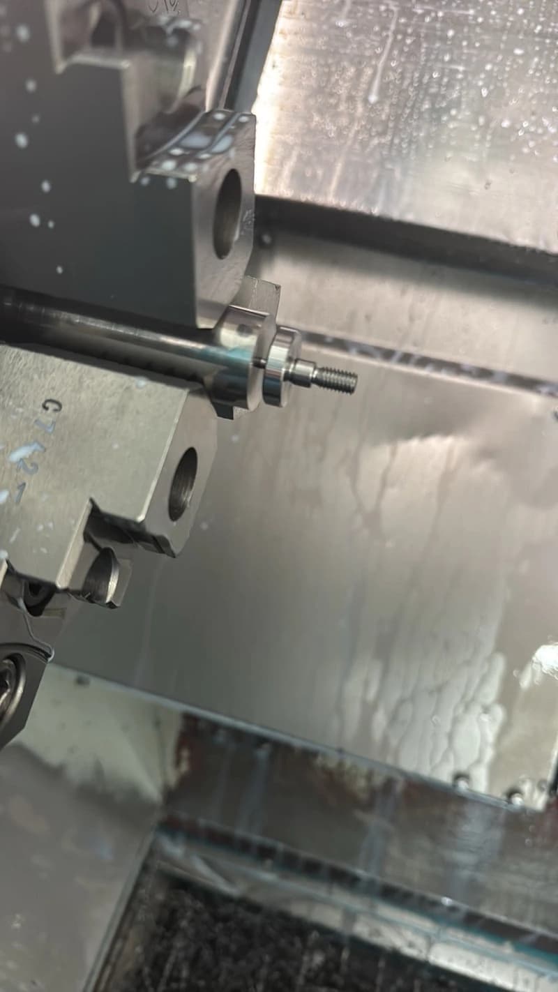 Nahaufnahme einer Drehmaschine bei der Metallbearbeitung, wobei ein Werkstück eingespannt ist. Die Maschine ist mit Kühlmittel bedeckt.