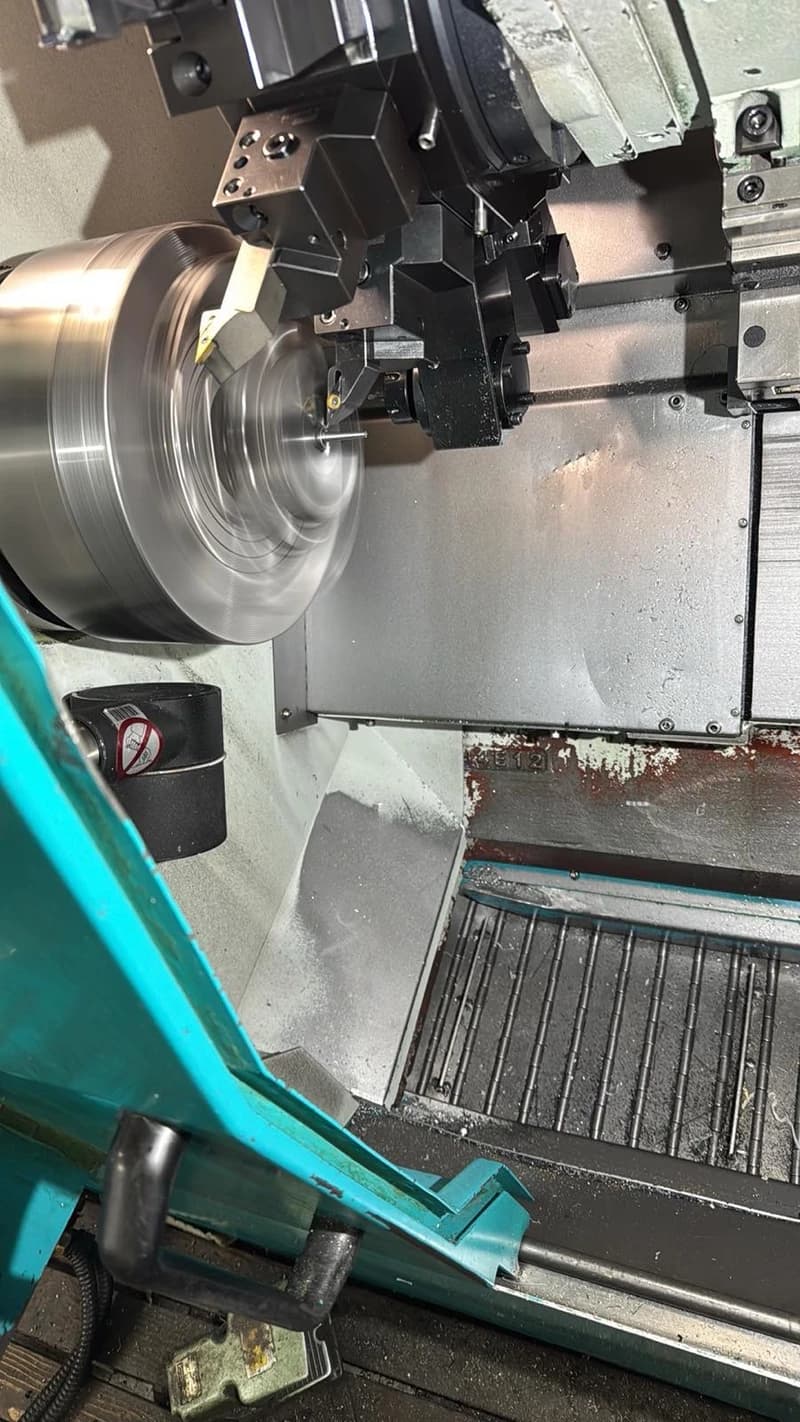 Eine Drehmaschine bearbeitet ein Metallstück. Die Maschine ist in Betrieb und spritzt Kühlmittel.