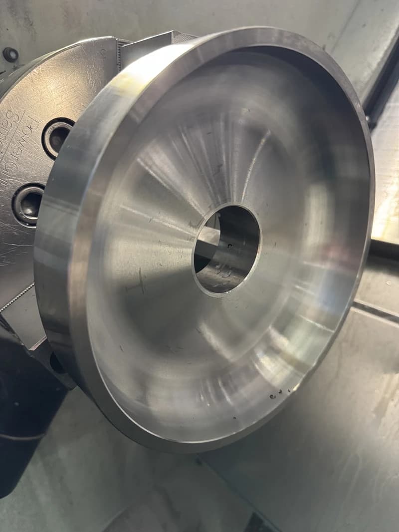 Nahaufnahme eines metallischen Werkstücks, das in einer Drehmaschine bearbeitet wird. Das Werkstück hat eine zylindrische Form mit einer zentralen Bohrung.